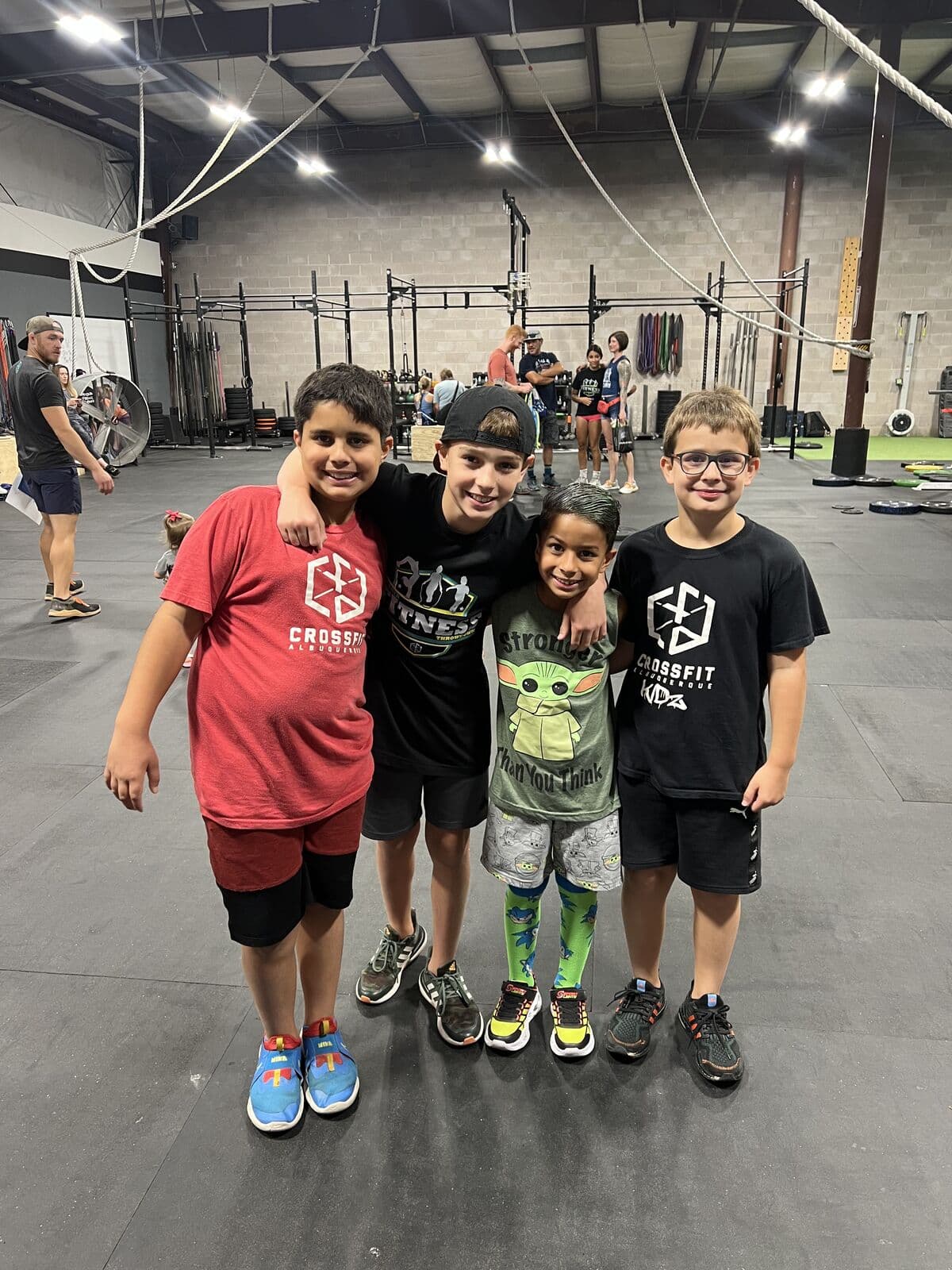 Four CrossFit Kids members with their arms around each other on the gym floor at CrossFit Albuquerque